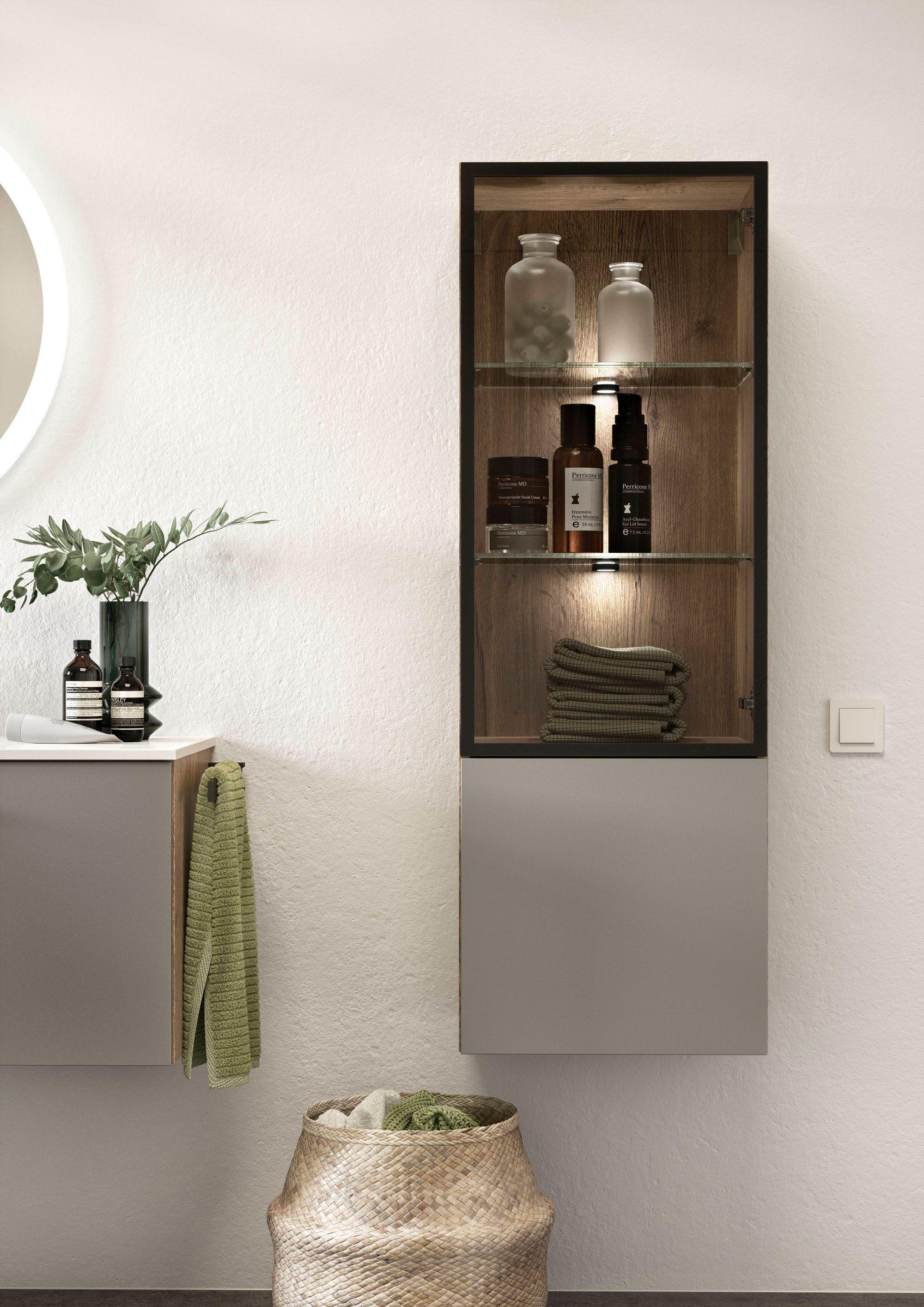 Detailansicht eines eleganten Badezimmerschranks mit beleuchteten Glasregalen und dekorativer Einrichtung. Bild 2: Modernes Badezimmer mit ovalem beleuchtetem Spiegel, Holz- und Grautönen sowie einer stilvollen Regalkombination.