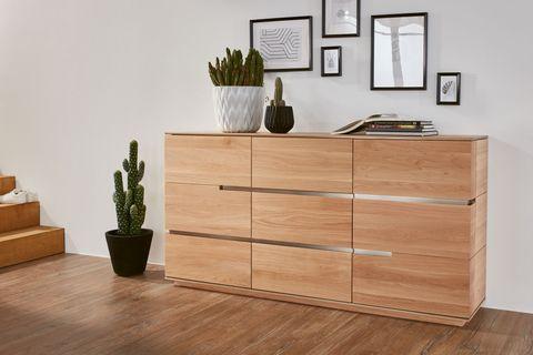 Moderne Holzkommode mit klaren Linien, dekoriert mit Pflanzen und eingerahmten Bildern, auf einem warmen Holzfußboden.