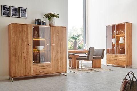 Elegante Holzvitrinen mit beleuchteten Glaselementen und integriertem Stauraum, kombiniert mit einem modernen Essbereich und grauen Polsterstühlen.