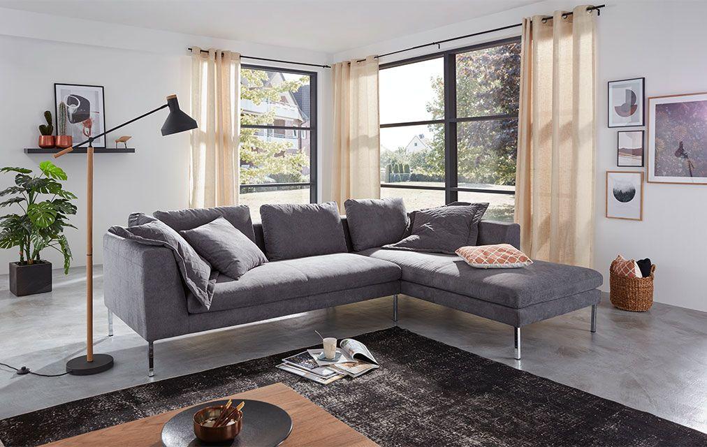 Ein modernes Wohnzimmer mit einer grauen Eckcouch, die mit mehreren Kissen dekoriert ist, einer Stehlampe und einem Couchtisch.