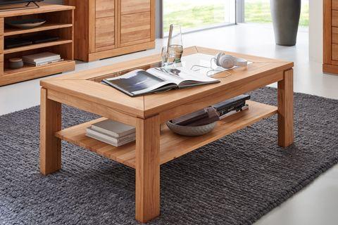 Massiver Couchtisch aus Holz mit Glasplatte und Ablagefach, dekoriert mit Büchern und einem Glas Wasser, auf einem grauen Teppich.