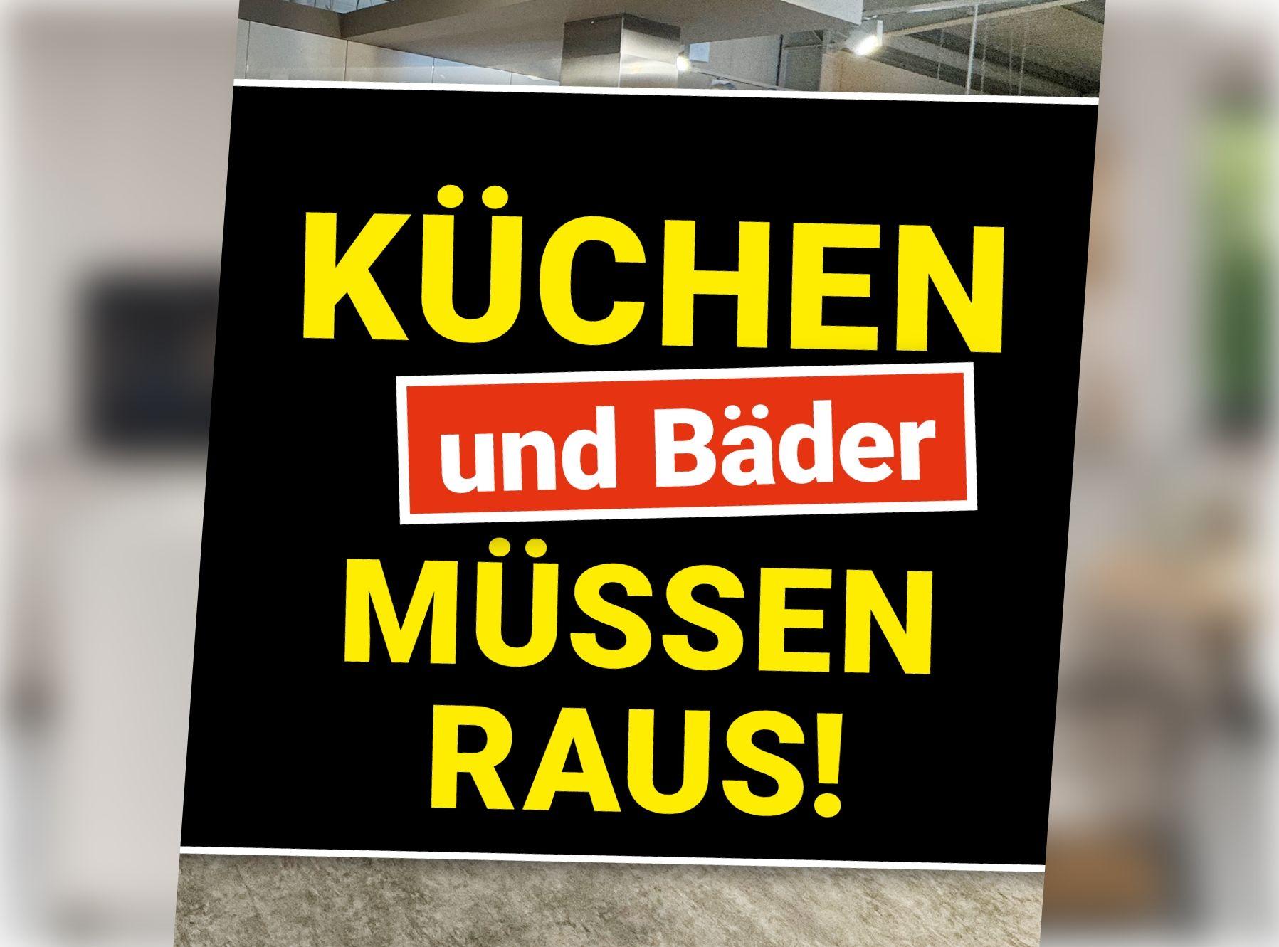 Schwarzes Aktionsbanner mit gelber Schrift vor leerem Ausstellungsraum. Schriftzug: „Küchen und Bäder müssen raus!"
