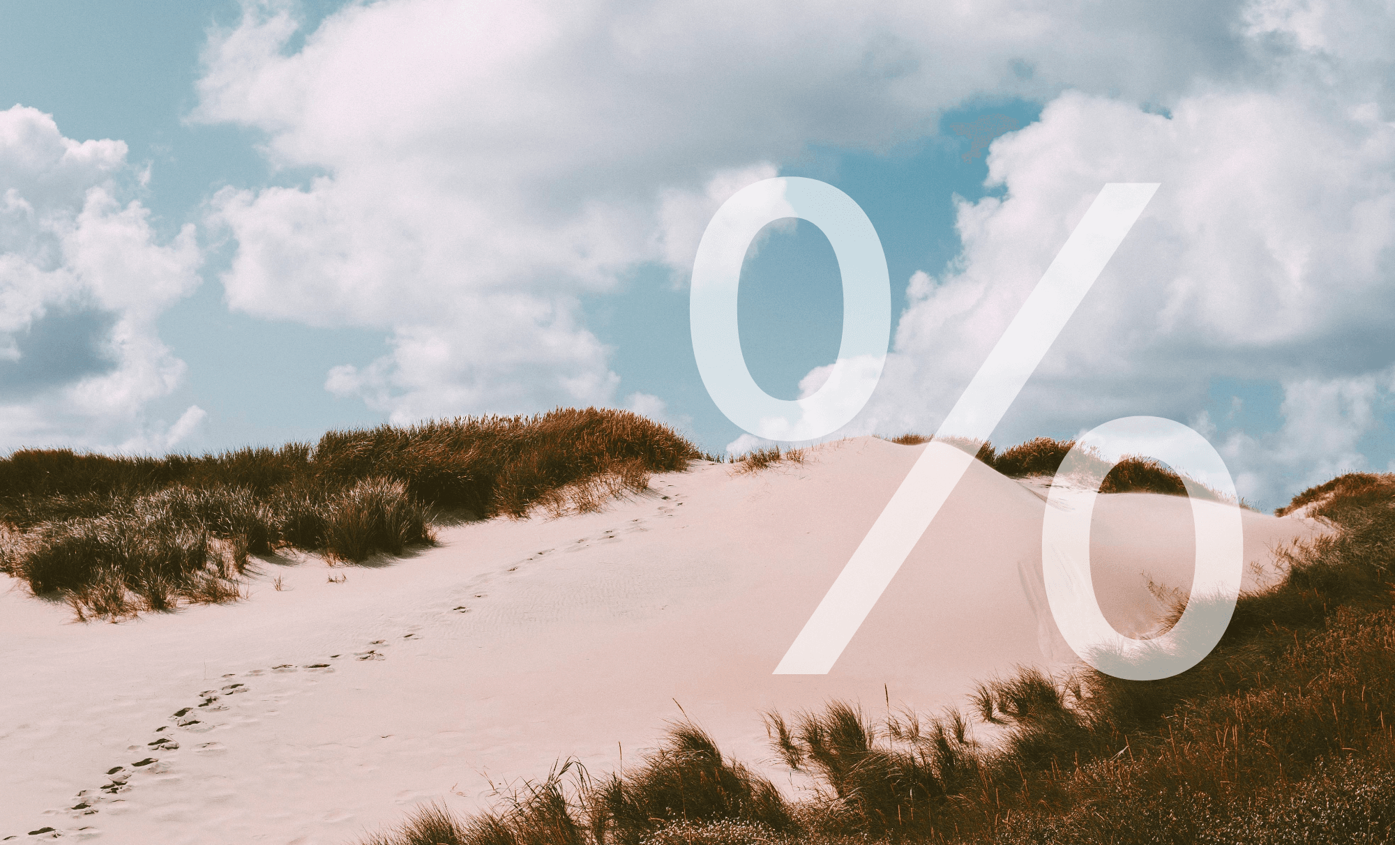 Sanddünenlandschaft mit weißem Sand, Dünen-bewachsenen Gräsern, Fußspuren im Sand und bewölktem Himmel im Hintergrund