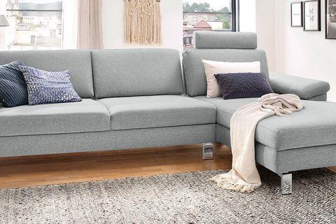 Helles Ecksofa in modernem Design mit grauem Stoffbezug und Kissen, ergänzt durch eine gemütliche Wohnzimmereinrichtung.