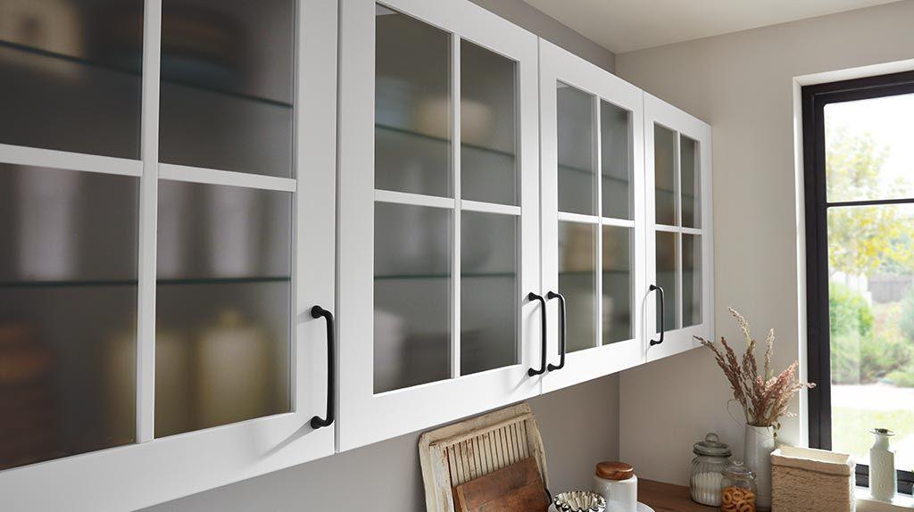 Nahaufnahme von weißen Küchenschränken mit Glaseinsätzen und schwarzen Griffen, die eine elegante und moderne Optik vermitteln.