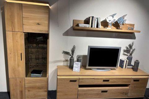 Wohnwand aus hellem Holz mit natürlicher Maserung. Links ein Schrank mit Glastür und Holzfächern, rechts ein TV-Board mit Fernseher und Schubladen. Darüber ein schlichtes Wandregal mit Büchern und dekorativen Fischen.