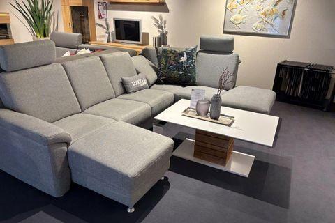 Stilvolle Couchgarnitur Calma in hellem Grau mit modernen Kissen und einem runden Holztisch, dekoriert in einem Showroom.