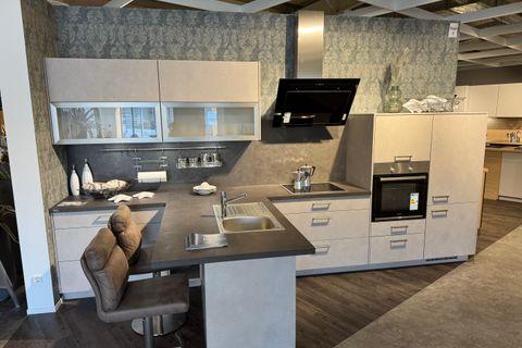 Einbauküche in hellem Sandton mit dunkler Arbeitsplatte, Halbinsel mit Barhockern, Glasoberschränken und schwarzer Schräghaube