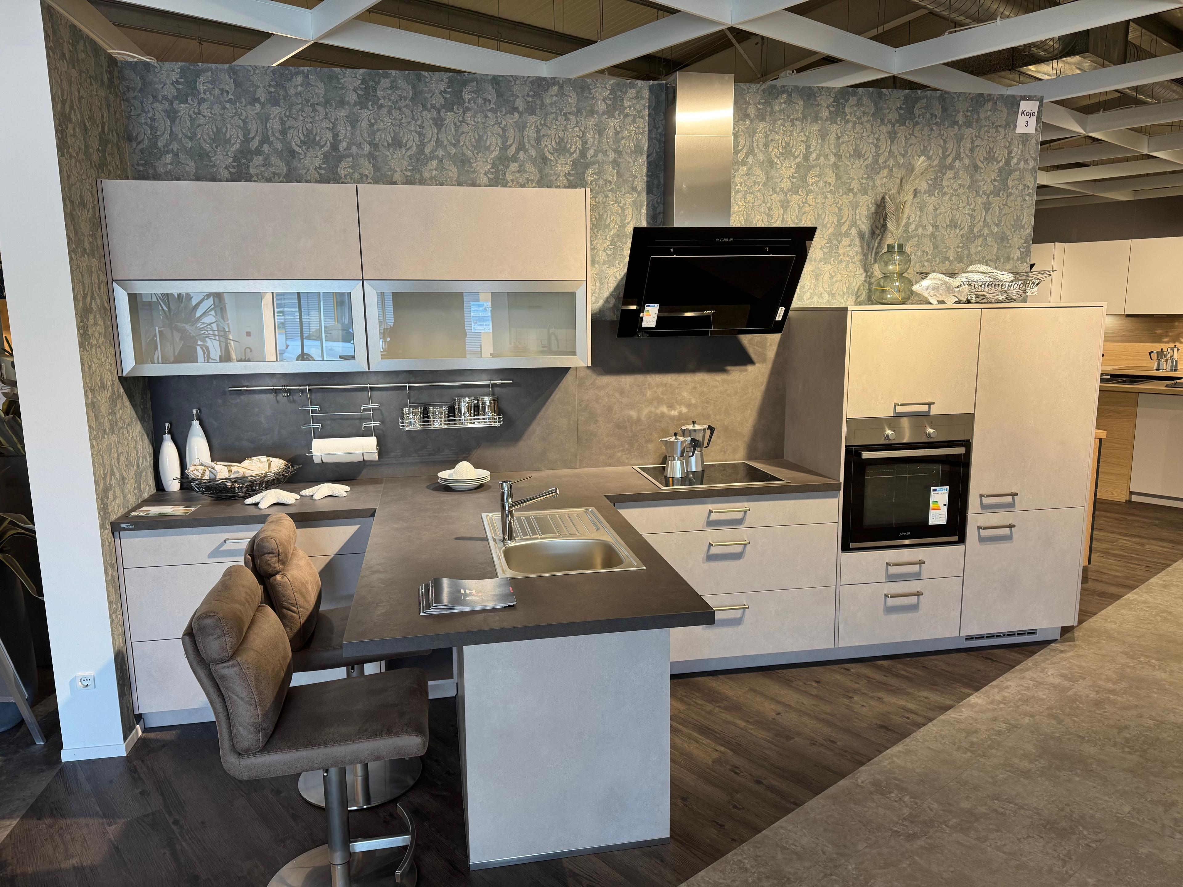 Einbauküche in hellem Sandton mit dunkler Arbeitsplatte, Halbinsel mit Barhockern, Glasoberschränken und schwarzer Schräghaube