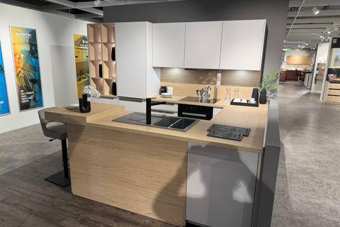 Moderne Küche in Weiß und Grau mit großer Kochinsel in Holzoptik, integriertem Kochfeld mit Downdraft-Abzug, schwarzer Armatur und offenem Holzregal