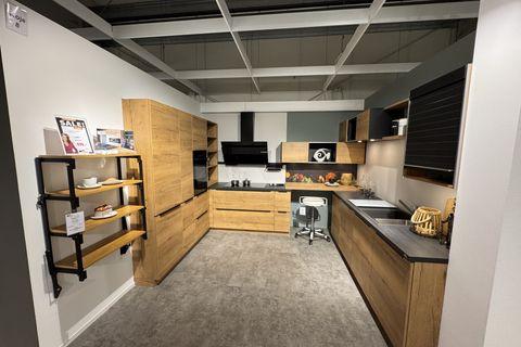 Küche in Eiche-Nachbildung mit schwarzer Arbeitsplatte, schwarzer Schräghaube, grifflosen Fronten, offenem Metallregal und dekorativer Nischenrückwand in U-Form.