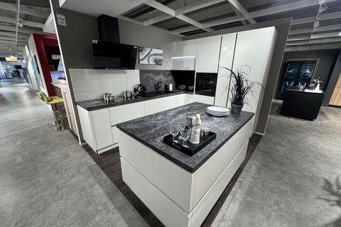 Hochglanz-Küche in Weiß mit grifflosen Fronten, dunkler Naturstein-Arbeitsplatte, freistehender Kochinsel, schwarzer Schräghaube und integriertem Geräteschrank