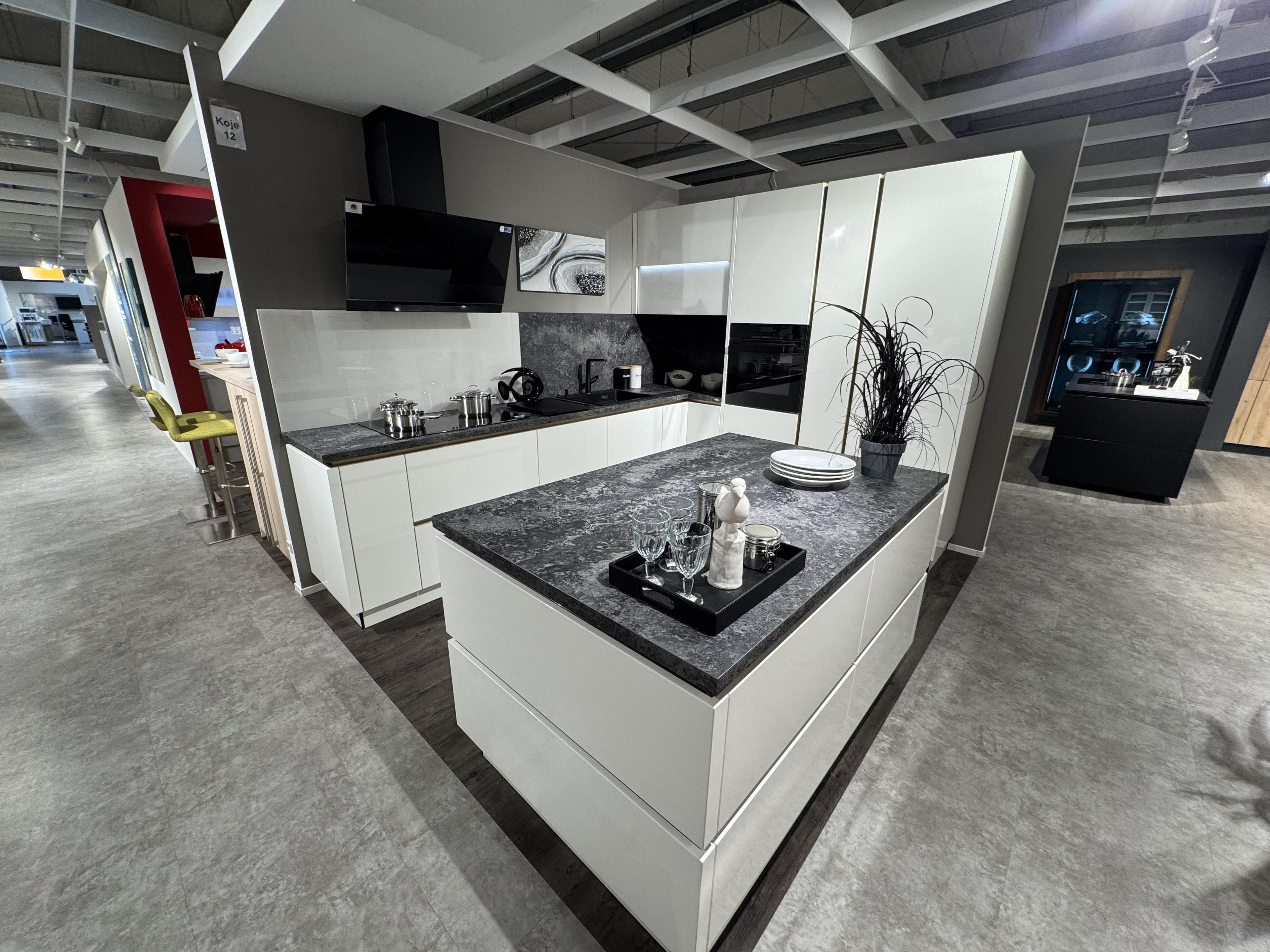 Hochglanz-Küche in Weiß mit grifflosen Fronten, dunkler Naturstein-Arbeitsplatte, freistehender Kochinsel, schwarzer Schräghaube und integriertem Geräteschrank