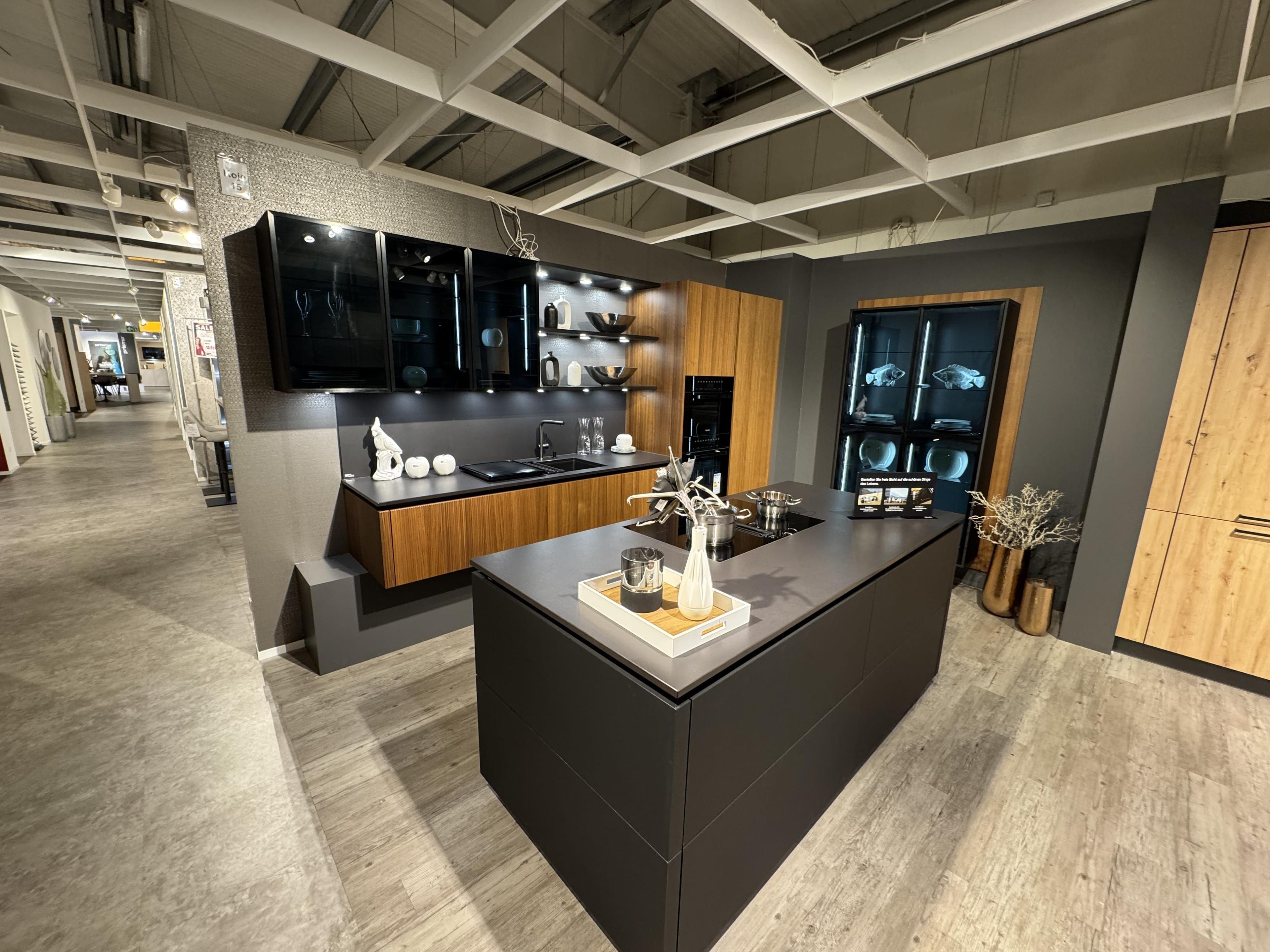 Elegante Küche in Mattschwarz und Nussbaum-Optik mit freistehender Kochinsel, beleuchteten Glasvitrinen, offenen Designregalen und integriertem Geräteschrank.