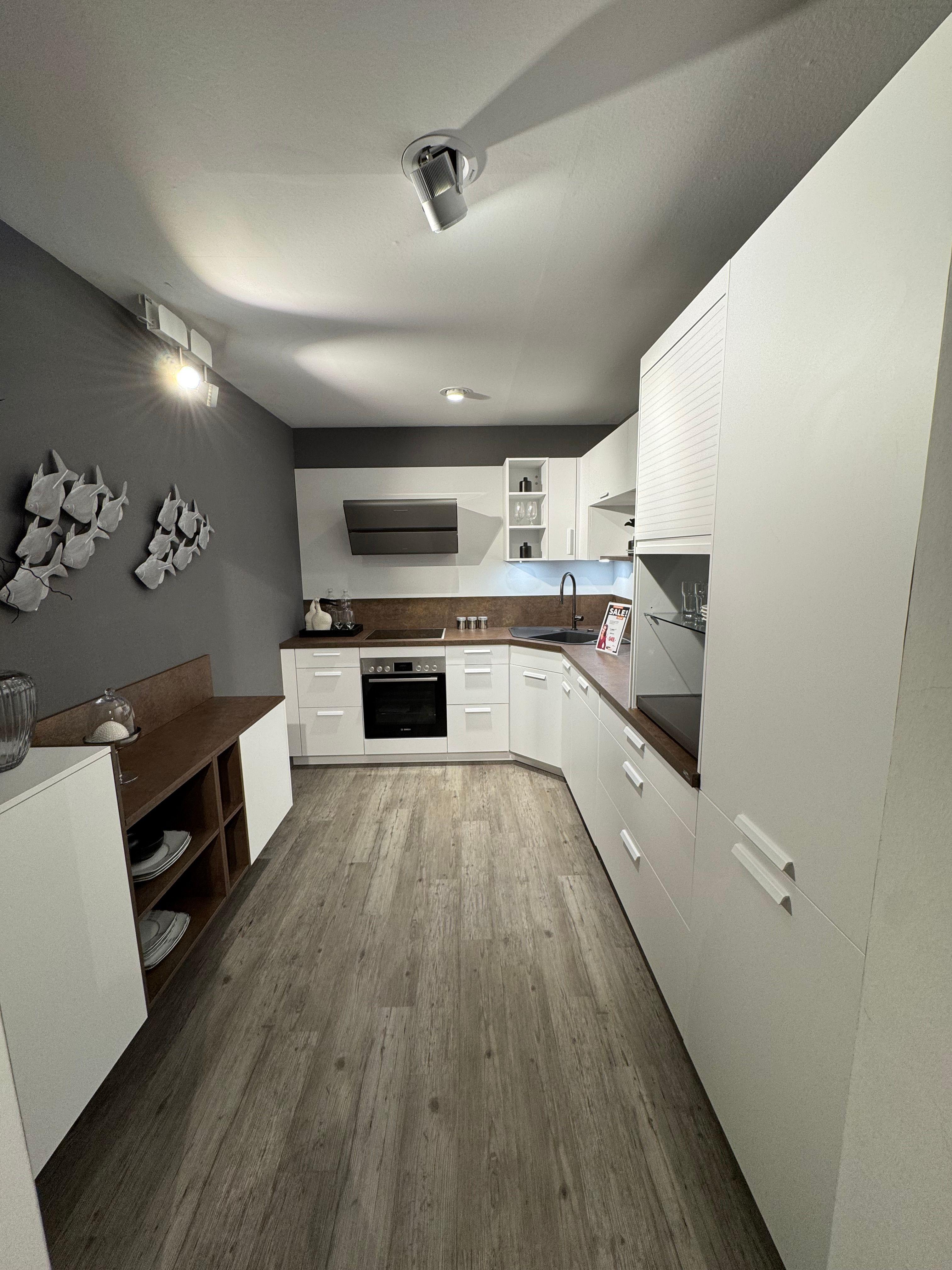 Weiße Einbauküche in L-Form mit Kupfer-Arbeitsplatte und passender Nischenrückwand, weißen Fronten mit Stangengriffen, Jalousieschrank und grauer Akzentwand mit dekorativer Fisch-Wanddeko