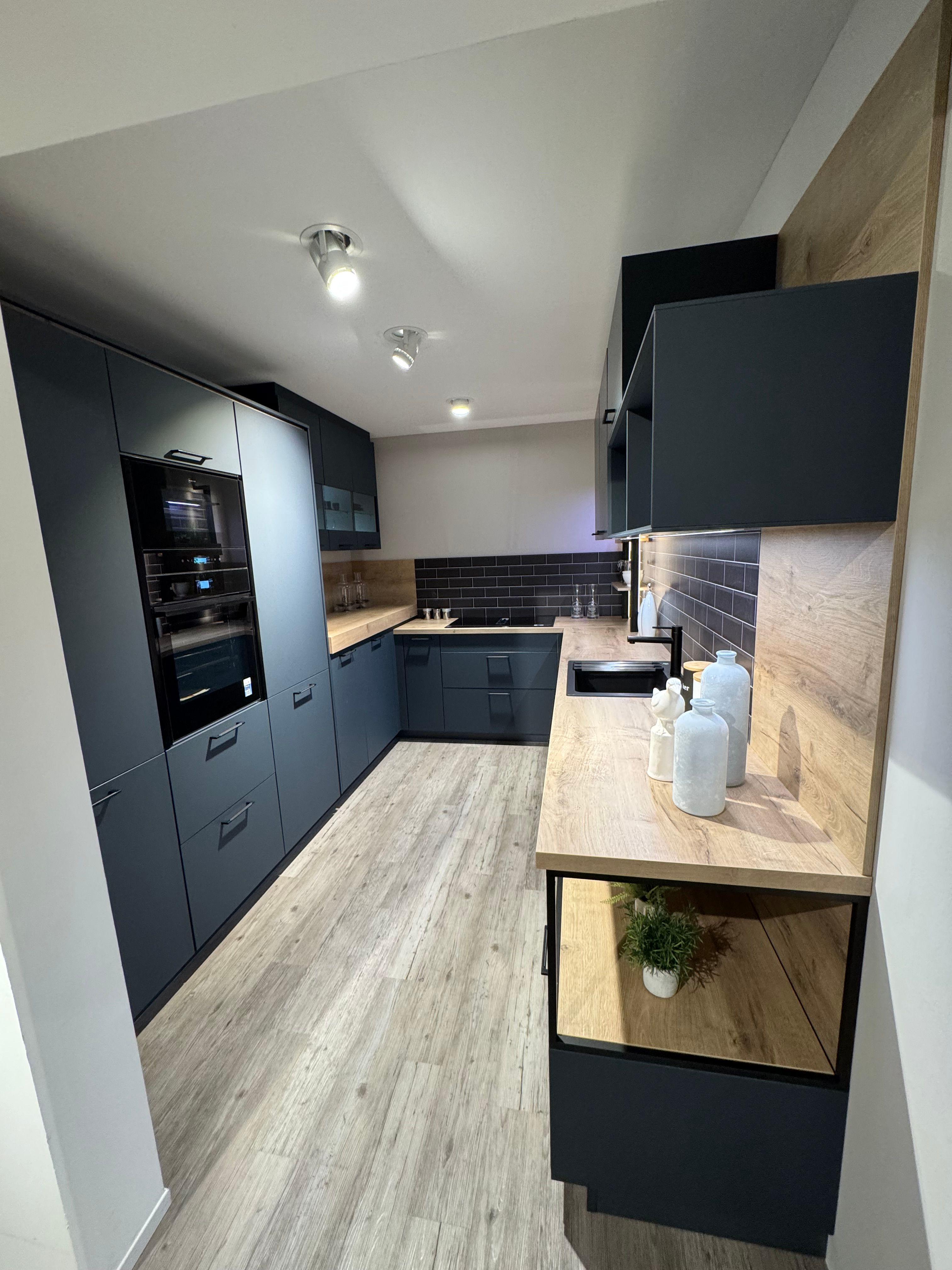 U-förmige Küche in mattem Petrolblau mit Holzarbeitsplatte in Eiche-Optik, dunklen Metro-Fliesen als Nischenrückwand, schwarzer Armatur, Hochschrank mit Einbaugeräten und offenem Metallregal mit Holzböden.