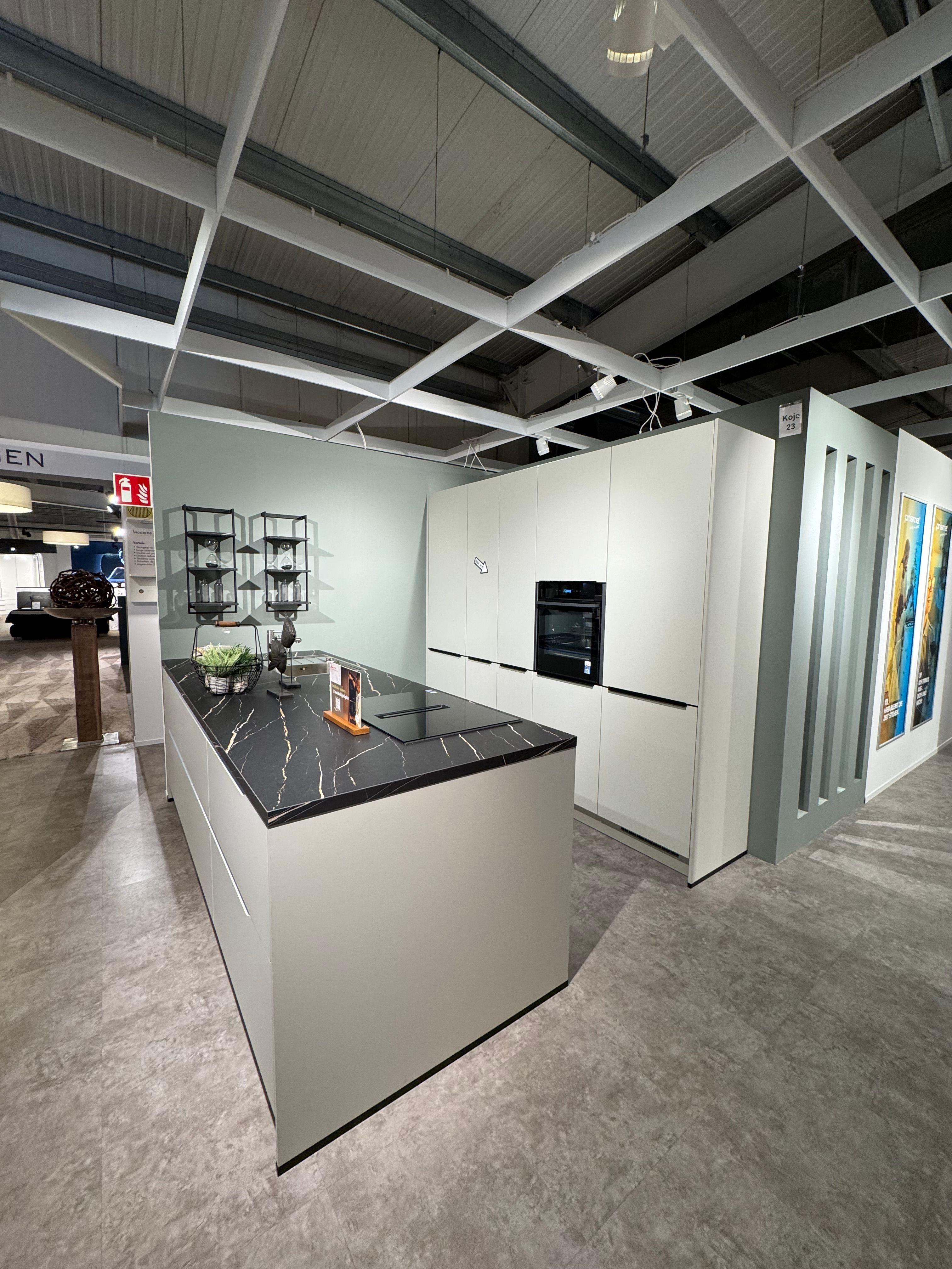 Minimalistische Küche in hellem Graugrün mit grifflosen Fronten, schwarzer Marmor-Arbeitsplatte mit weißer Maserung, großer Kochinsel mit Induktionskochfeld, Hochschrankzeile mit integrierten Geräten und offenem Metallregal.