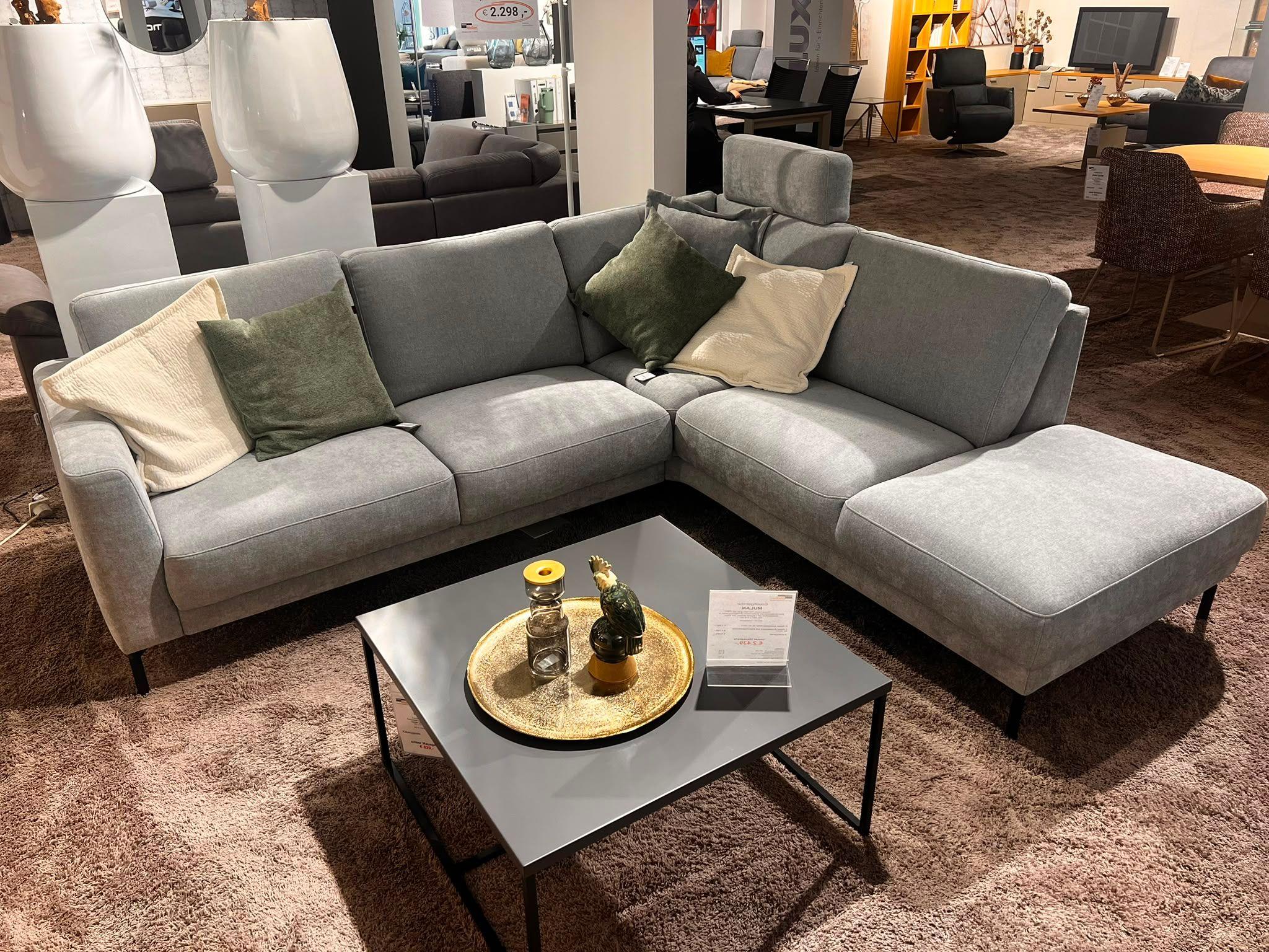 Graue Polstergarnitur als Eckkombination mit dunklem Couchtisch sowie Kissen in beige und tannengrün