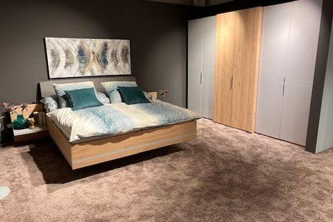 Modernes Schlafzimmer-Set mit schwebendem Bett aus hellem Holz und gepolstertem Kopfteil, dekoriert mit türkisfarbenen Kissen und passender Bettwäsche. Im Hintergrund ein großer Kleiderschrank in Weiß und Holz sowie eine Wanddekoration.