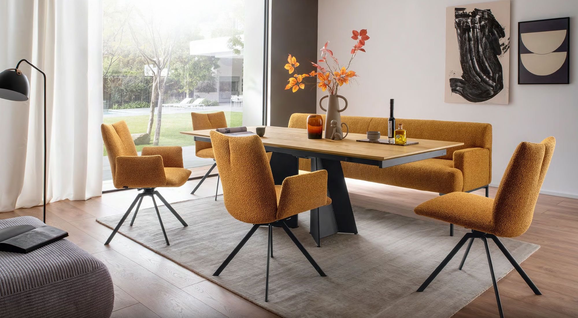 Modernes Esszimmer-Set mit einem Holztisch und orangefarbenen Polsterstühlen sowie einer passenden Bank. Dekoratives Highlight sind herbstliche Blumen in einer Vase auf dem Tisch.