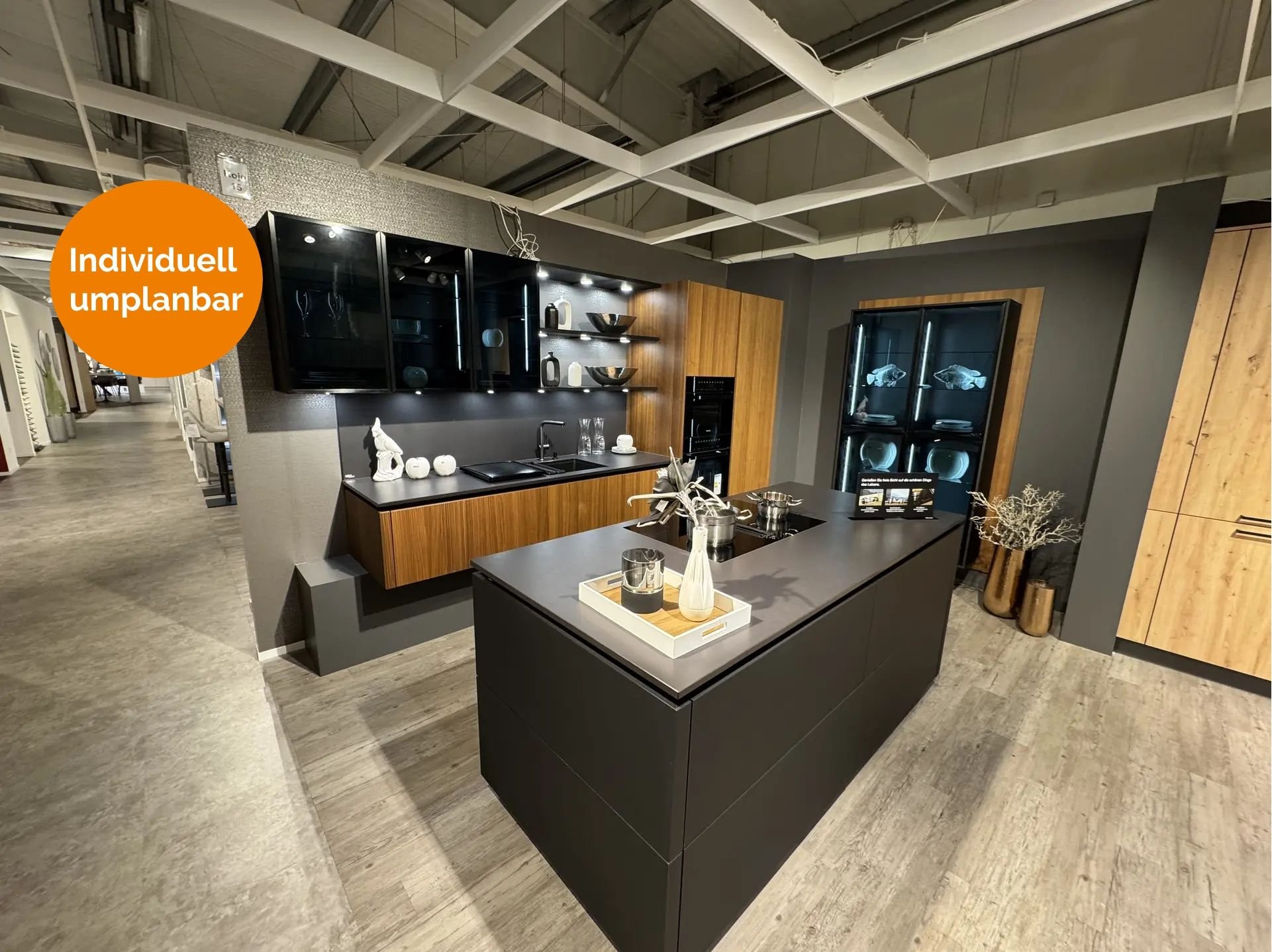 Elegante Küche in Mattschwarz und Nussbaum-Optik mit freistehender Kochinsel, beleuchteten Glasvitrinen, offenen Designregalen und integriertem Geräteschrank.