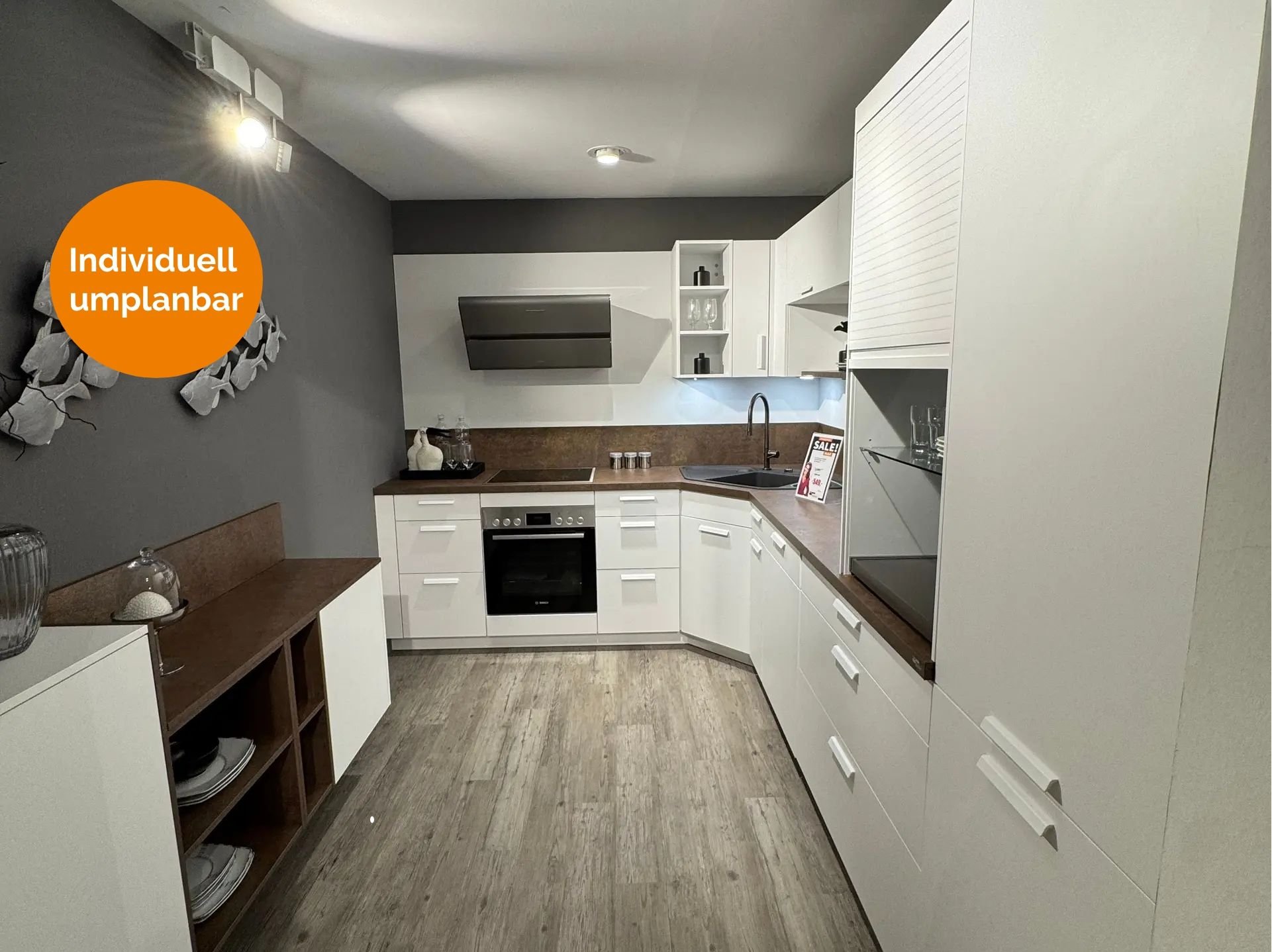 Weiße Einbauküche in L-Form mit Kupfer-Arbeitsplatte und passender Nischenrückwand, weißen Fronten mit Stangengriffen, Jalousieschrank und grauer Akzentwand mit dekorativer Fisch-Wanddeko