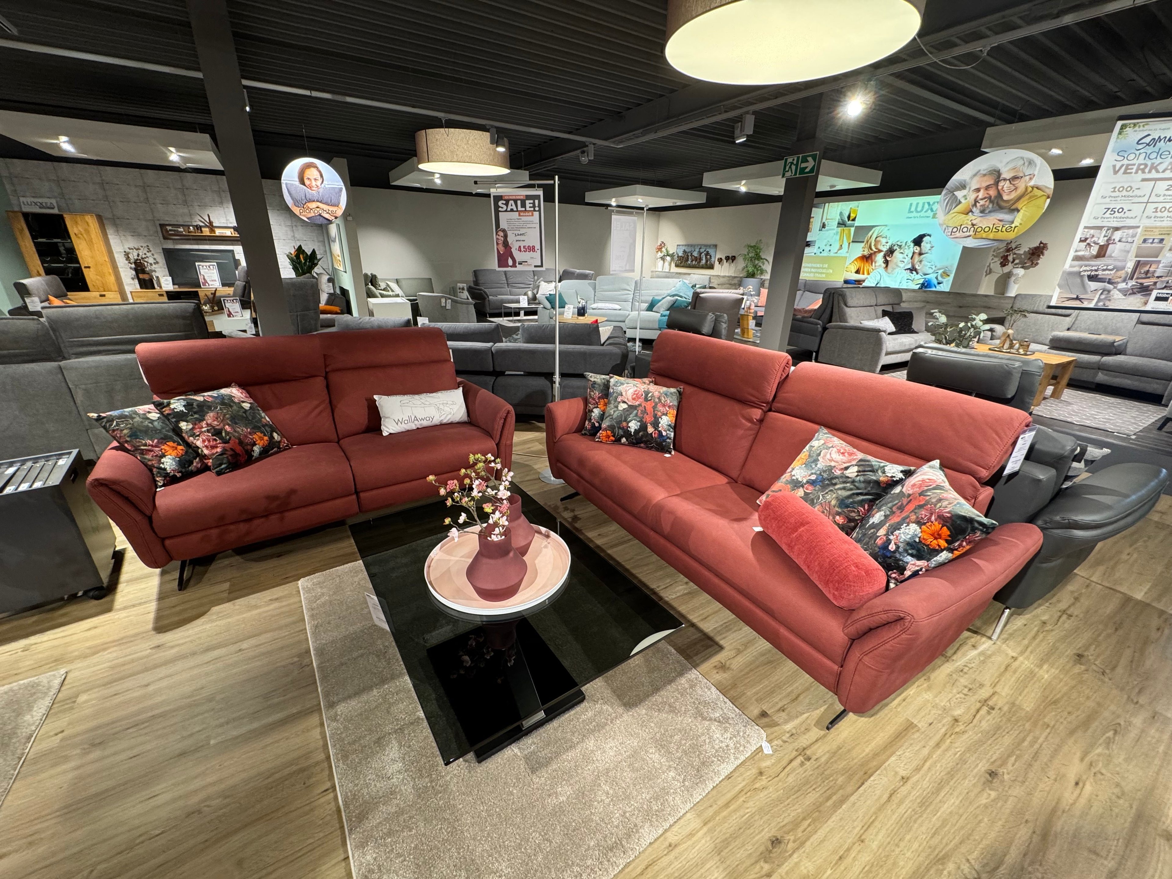 Zwei Sofas in rot mit Kissen mit Blümchenmuster und schwarzer Glastisch