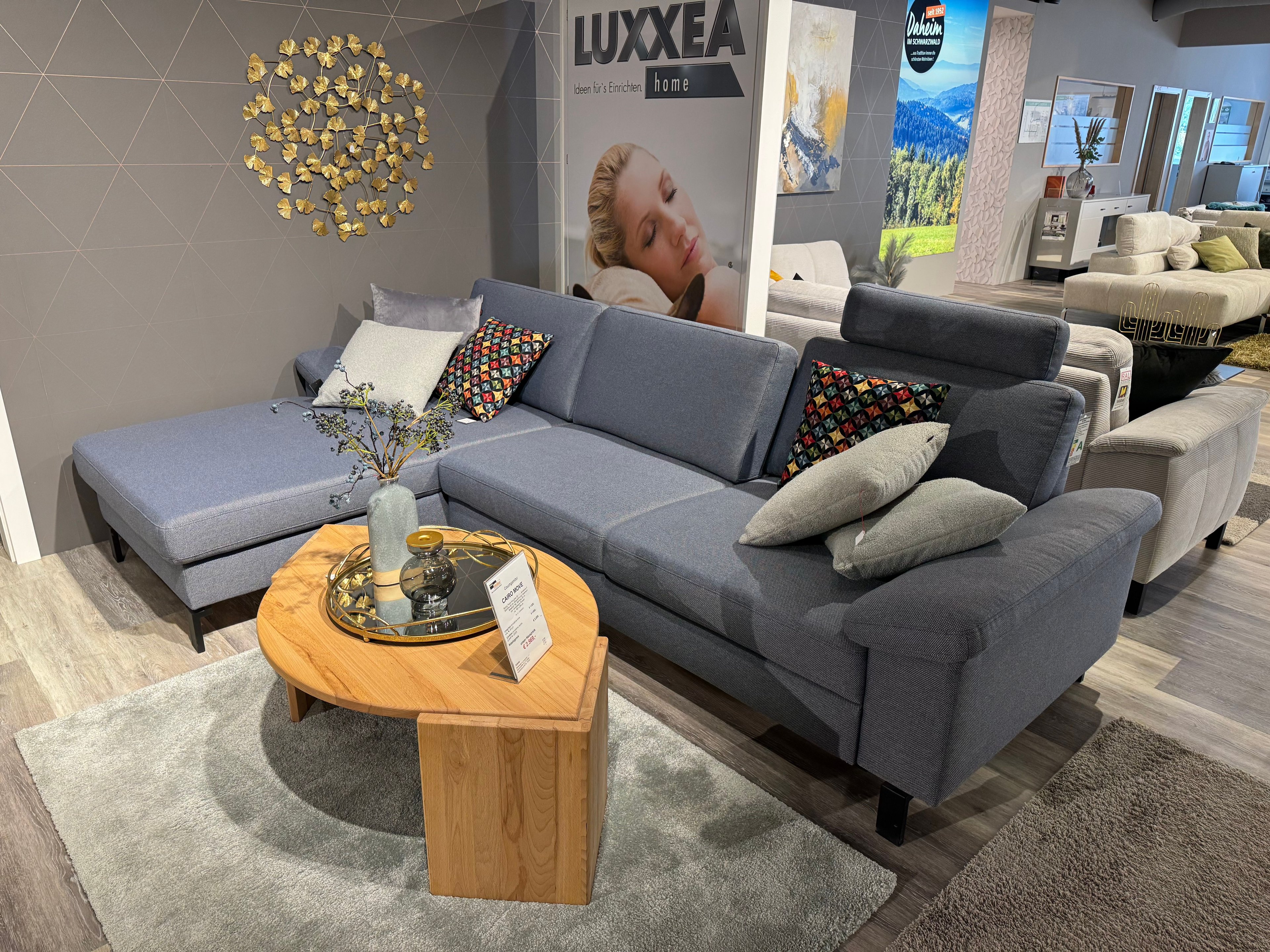 Couchgarnitur in L-Form mit blau-grauem Stoffbezug mit grauen und bunten Kissen