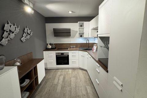 Weiße Einbauküche in L-Form mit Kupfer-Arbeitsplatte und passender Nischenrückwand, weißen Fronten mit Stangengriffen, Jalousieschrank und grauer Akzentwand mit dekorativer Fisch-Wanddeko