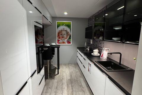 Küche in Weiß Hochglanz mit schwarzen Griffleisten, dunkler Arbeitsplatte, schwarzen Glas-Hängeschränken mit Innenbeleuchtung, Steinoptik-Nischenrückwand, schwarzer Armatur und kleinem Bartisch mit Hockern